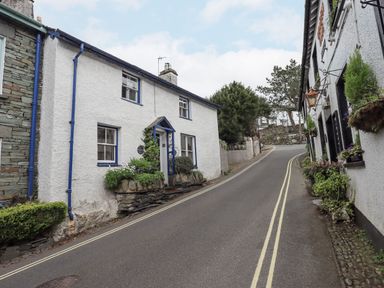 A narrow street with white buildings and plants along the sides at Springwell Cottage in Ambleside