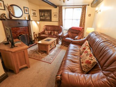 A living room with brown leather sofas a wooden coffee table a fireplace and a television at Springwell Cottage in Ambleside