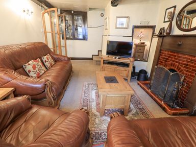 A living room with brown leather sofas a wooden coffee table television and a fireplace at Springwell Cottage in Ambleside