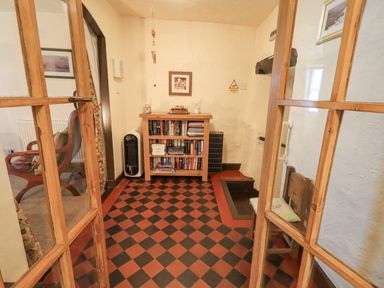 An entryway with a wooden bookshelf filled with books a patterned floor a wooden chair and double wooden framed glass doors