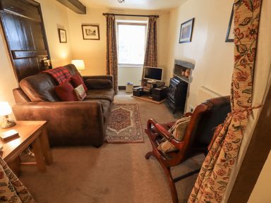A living room with a brown leather sofa two armchairs a wooden side table a small rug a television and a fireplace at Springwell Cottage in Ambleside