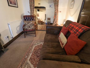 A living room with a brown sofa and red pillows next to an armchair and a rug at Springwell Cottage in Ambleside