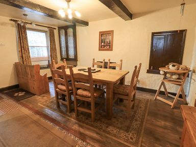 A dining room with a wooden table surrounded by chairs and a bench with cushions at Springwell Cottage in Ambleside