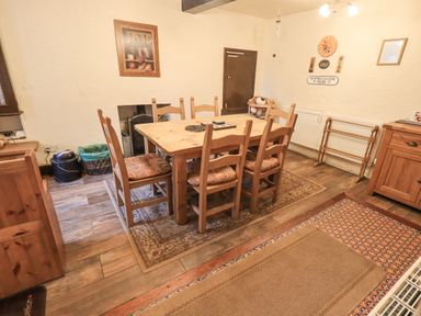 A dining room with a wooden table and six chairs on rugs with wooden cabinets and framed pictures on walls at Springwell Cottage in Ambleside