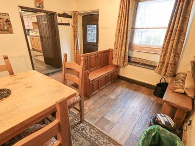 A dining area with wooden table and chairs a wooden bench near a window with floral curtains and a view outside at Springwell Cottage Ambleside