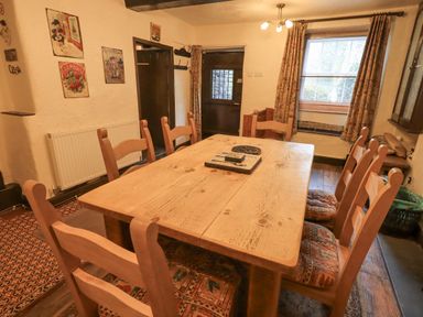 A dining room with a wooden table and eight wooden chairs with patterned cushions at Springwell Cottage in Ambleside