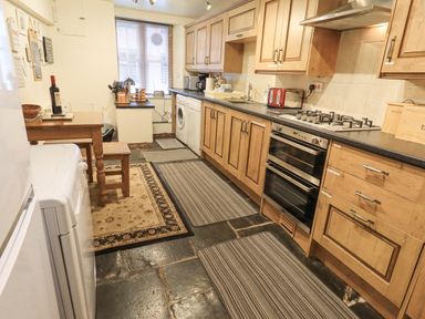A kitchen with wooden cabinets a gas stove oven a washing machine a table and a window at Springwell Cottage in Ambleside