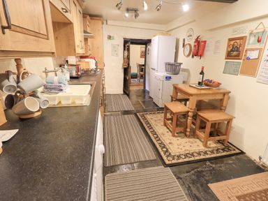 A kitchen with wooden cabinets a countertop sink a refrigerator a small wooden table with two stools and rugs on the floor at Springwell Cottage in Ambleside