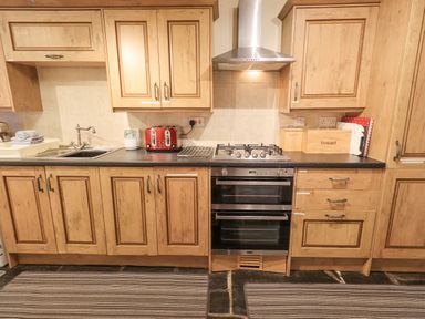 A kitchen with wooden cabinets a gas stove a sink a red toaster and a bread box at Springwell Cottage in Ambleside