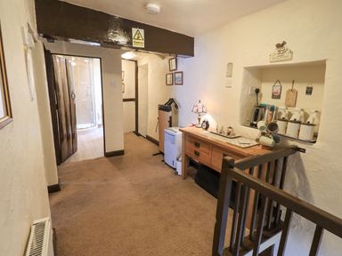 A hallway with a wooden side table holding a lamp and cups a radiator and a bathroom visible through a door at Springwell Cottage in Ambleside