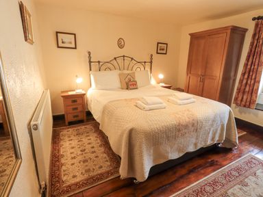 A bedroom with a double bed with white linens two bedside tables with lamps a wooden wardrobe patterned rugs and curtains at Springwell Cottage in Ambleside