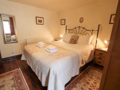 A bedroom with a double bed two bedside tables with lamps and framed pictures on the walls at Springwell Cottage in Ambleside