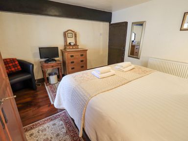 A bedroom with a bed with folded towels a wooden chest of drawers a small table with a TV and a black armchair at Springwell Cottage in Ambleside