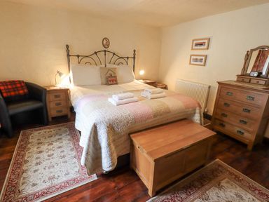 A bedroom with a bed with folded towels bedside tables a chair a wooden chest and a dresser with mirror at Springwell Cottage Ambleside