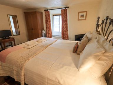 A bedroom with a large bed, folded towels, a wardrobe, a small table with a TV, and a window with curtains at Springwell Cottage in Ambleside