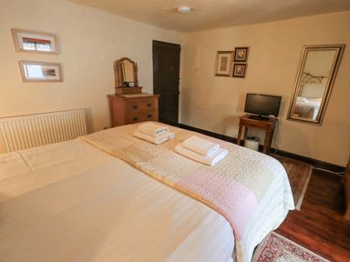 A bedroom with a made bed topped with folded towels a wooden dresser a small table with a television and a wall mirror at Springwell Cottage in Ambleside