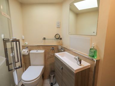 A bathroom with a toilet a sink with cabinet a mirror a glass shelf and a shower at Springwell Cottage in Ambleside