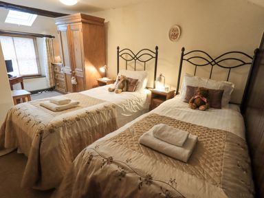A bedroom with two single beds each with a teddy bear and folded towels a wooden wardrobe a chest of drawers and a desk with a chair at Springwell Cottage in Ambleside