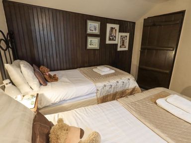 A bedroom with two single beds each with folded towels and teddy bears and dark wood paneled wall at Springwell Cottage in Ambleside
