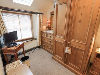 A bedroom with wooden wardrobe and dresser a small table with a TV and window with blinds and curtains at Springwell Cottage in Ambleside