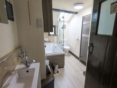 A bathroom with a sink and faucet a bathtub with a glass screen a toilet a radiator and a skylight at Springwell Cottage Ambleside