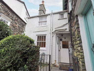 The exterior of a white cottage with stone walls a small garden area and a white door with a window at Springwell Cottage in Ambleside