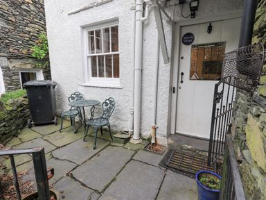 An outdoor patio area with a small metal table and two chairs a white door with a glass panel and a black metal gate at Springwell Cottage Ambleside