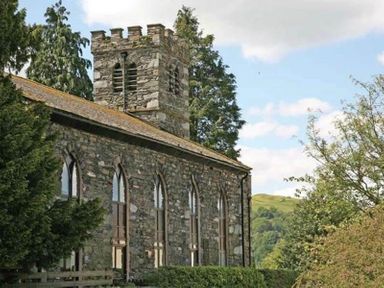 A stone church building with arched windows and a tower surrounded by trees at Candleberry Cottage in Ambleside