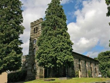 A stone building with a tower and arched windows among tall trees at Candleberry Cottage in Ambleside