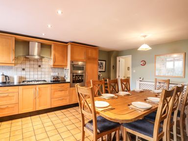 A kitchen with wooden cabinets and a dining table set with plates and cutlery at Candleberry Cottage in Ambleside
