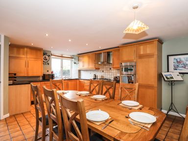 A kitchen with wooden cabinets a dining table set with plates and cutlery and a stand with open books at Candleberry Cottage in Ambleside