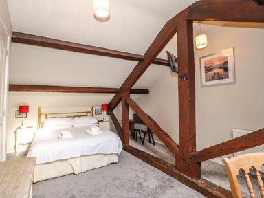 A bedroom with a bed and bedside tables under a sloped ceiling with exposed wooden beams at Candleberry Cottage in Ambleside
