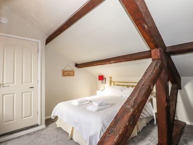 A bedroom with a double bed white bedding folded towels wooden beams on ceiling and walls at Candleberry Cottage in Ambleside