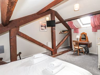 A bedroom with exposed wooden beams a bed with white towels a small dressing table and a chair at Candleberry Cottage in Ambleside