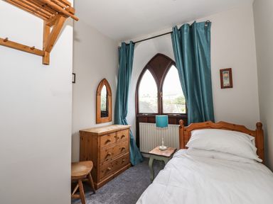 A bedroom with a wooden bed a wooden chest of drawers and a window with blue curtains at Candleberry Cottage in Ambleside