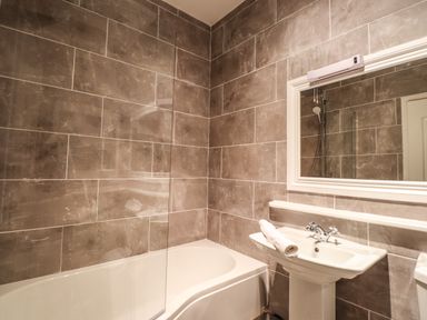 A bathroom with a bathtub a sink with a rolled towel and a mirror on the wall at Candleberry Cottage in Ambleside