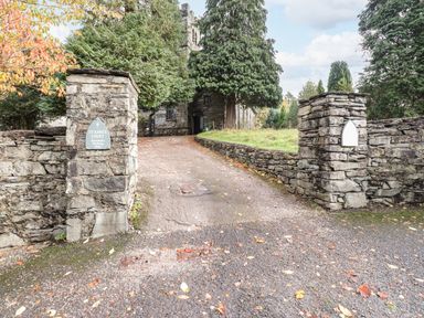A stone driveway entrance with stone pillars and walls leading to a stone building surrounded by trees at Candleberry Cottage in Ambleside
