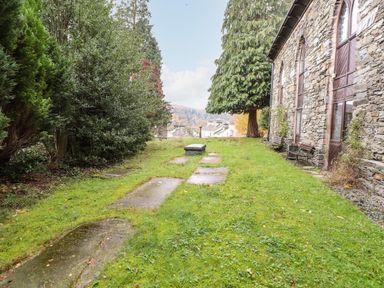 A grassy area with gravestones beside a stone building with benches at Candleberry Cottage in Ambleside