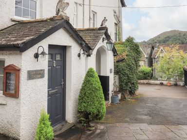 Exterior view of a white cottage with a dark door and small trees near the entrance at Gale Lodge Cottage in Ambleside