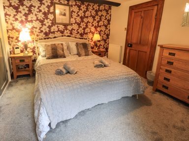 A bedroom with a double bed two bedside tables with lamps a wooden door and a chest of drawers at Gale Lodge Cottage in Ambleside