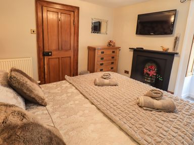A bedroom with a bed with folded towels a wooden door a chest of drawers and a wall-mounted TV at Gale Lodge Cottage in Ambleside