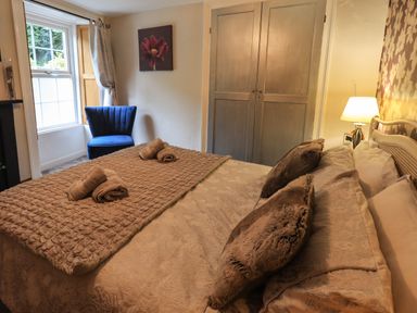 A bedroom with a bed and folded towels on it a blue chair near the window and a wooden wardrobe at Gale Lodge Cottage in Ambleside