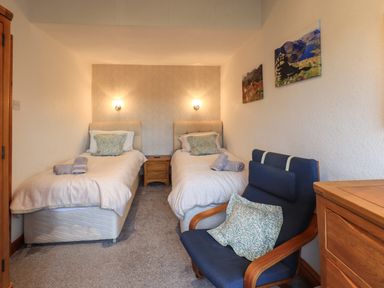 A bedroom with two single beds a blue armchair and wooden furniture at Gale Lodge Cottage in Ambleside