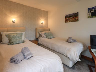 A bedroom with two single beds each with pillows and rolled towels next to a wooden nightstand at Gale Lodge Cottage in Ambleside