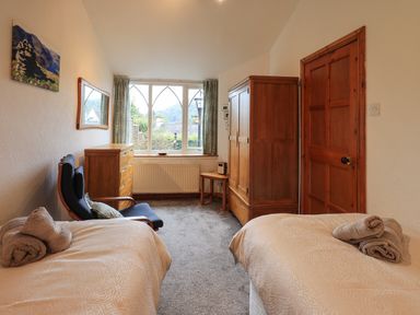 A bedroom with two single beds a wooden wardrobe chest of drawers and a chair by a window at Gale Lodge Cottage in Ambleside