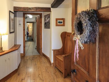 A hallway with wooden floor a wooden bench a sideboard with a lamp and framed pictures on the walls at Gale Lodge Cottage in Ambleside