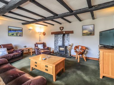 A living room with leather sofas a wooden coffee table a wood burning stove and a television at Gale Lodge Cottage in Ambleside