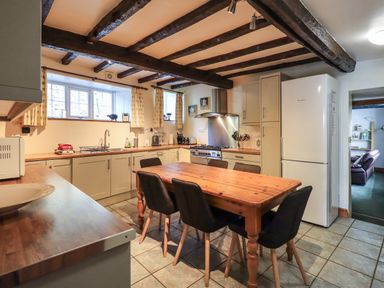 A kitchen with wooden table and six chairs white cabinets and black ceiling beams at Gale Lodge Cottage in Ambleside