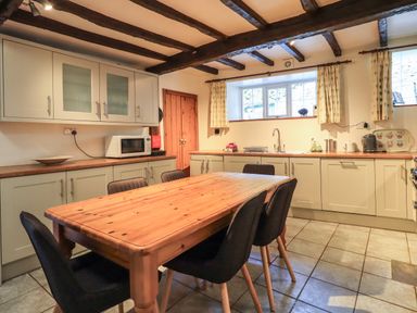 A kitchen with wooden dining table six black chairs cabinets a microwave and windows at Gale Lodge Cottage in Ambleside