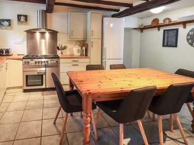 A kitchen with a wooden dining table chairs stove refrigerator and wall-mounted shelf at Gale Lodge Cottage in Ambleside